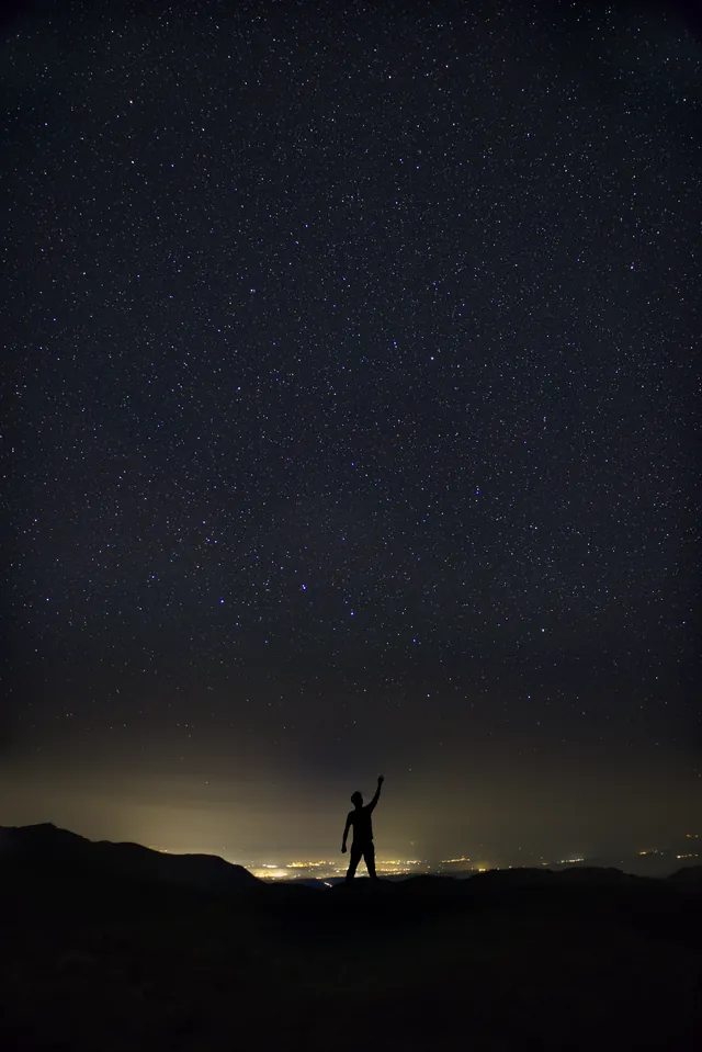A person silhouetted while reaching toward the stars
